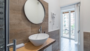 Un bagno con uno specchio rotondo, un lavabo bianco e una porta doccia in vetro.