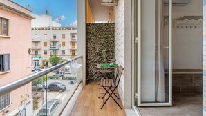 Un balcone con tavolo e sedie in legno, un muro in pietra e vista sulla strada sottostante.
