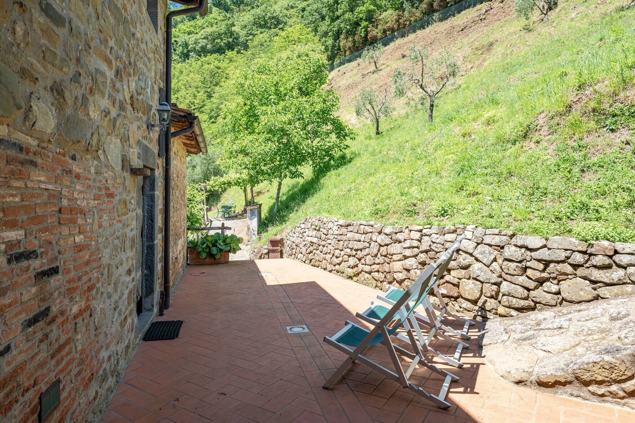 A stone wall, a brick building, and a paved area with chairs.