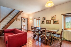 Un coin repas avec des chaises et une table en bois, un canapé rouge, un escalier et des tableaux accrochés au mur.