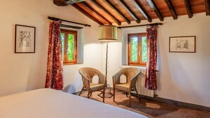 Una camera da letto con un letto, due poltrone in vimini, una lampada da terra e due finestre con tende.