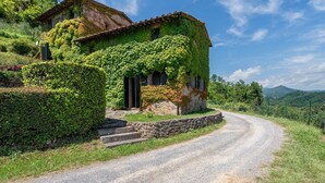 Una casa rustica con muri ricoperti d'edera, una scala in pietra e un vialetto sterrato.