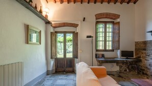 Una habitación acogedora con suelo de piedra, un banco de madera, un sofá con cojines, una pared de piedra y una ventana con vistas a la vegetación.