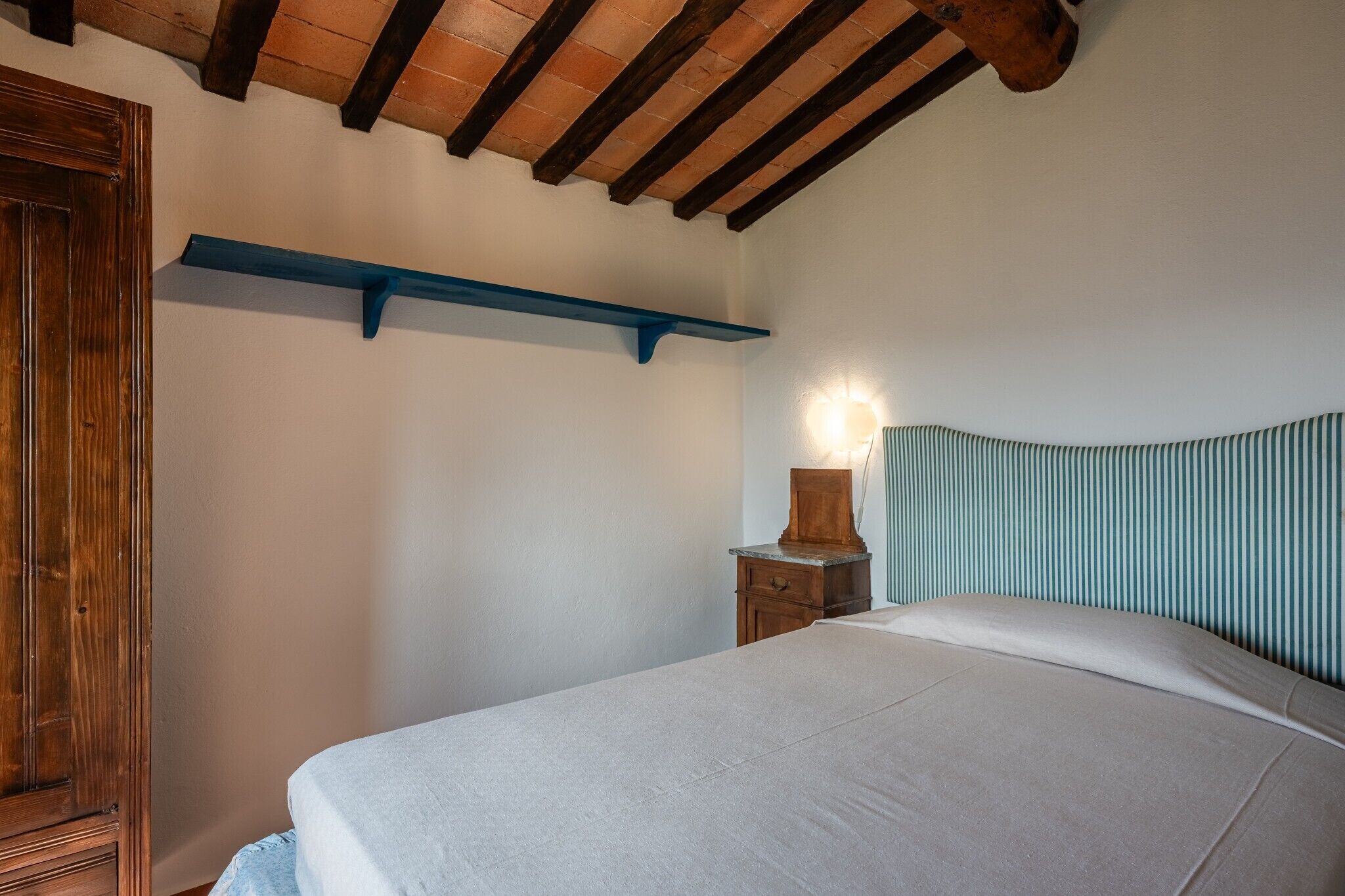 Ein Schlafzimmer mit einem Bett, einem Nachttisch, einer Lampe, einer Holztür und einem blauen Regal.