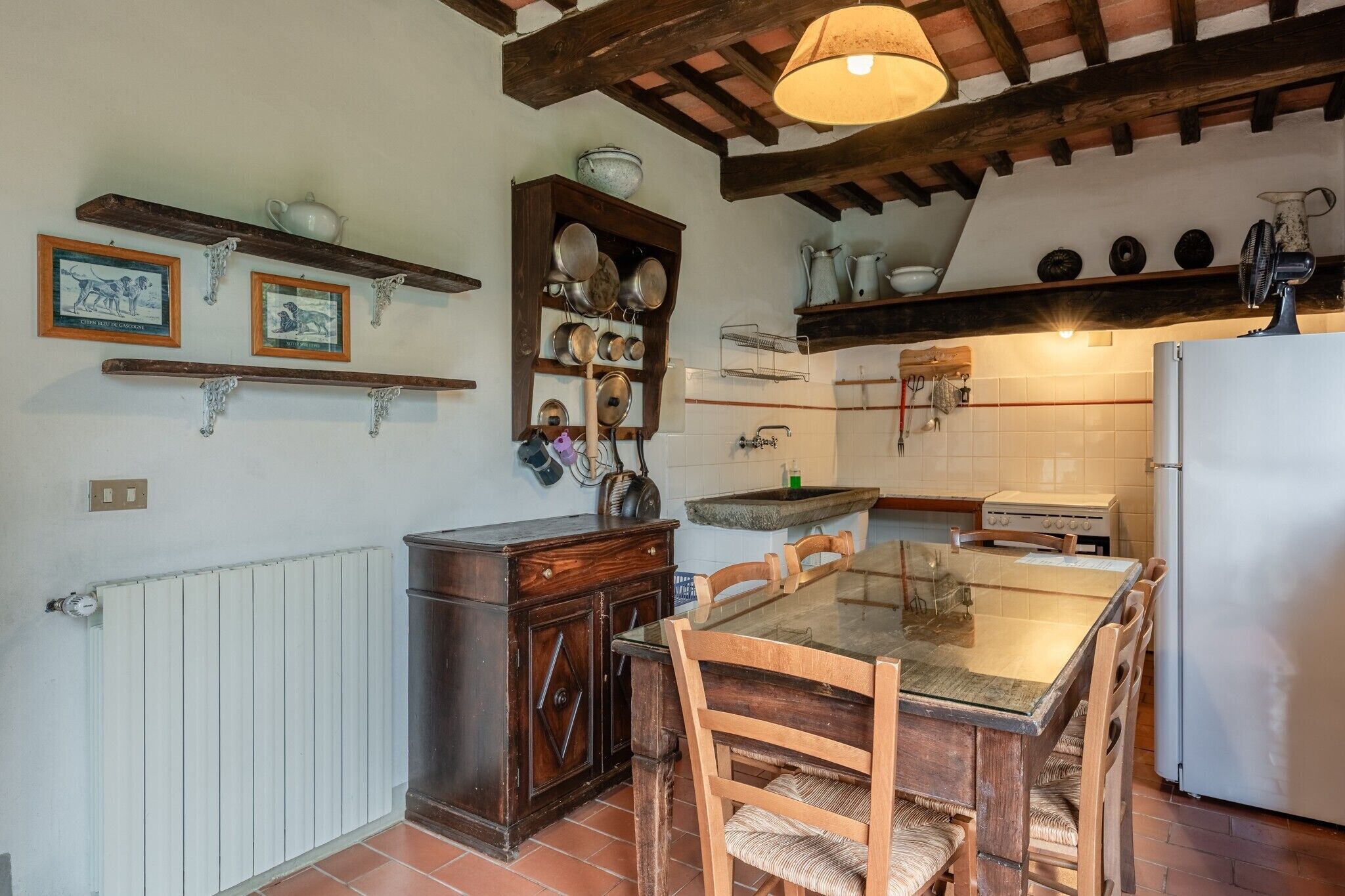 Una cocina con una mesa de madera, sillas, un refrigerador y diversos utensilios de cocina en estantes.