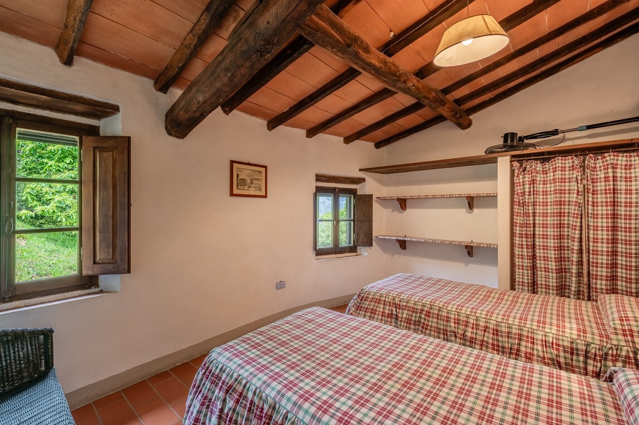 A room with two beds, wooden beams, a window, and a hanging lamp.
