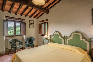 A bedroom with a bed, two chairs, a window with a view, and a lamp.