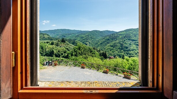 A view through an open window of a mountainous landscape with a paved area and railings.