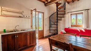 A kitchen with wooden cabinets, a sink, and a dining table with chairs. There is a red sofa and a spiral staircase.