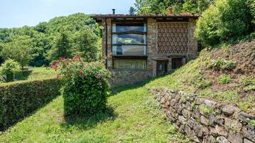 Edifici de pedra amb una finestra, envoltat de vegetació i un mur de pedra.