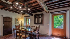 Comedor con mesa y sillas de madera, una lámpara de araña y vistas a follaje a través de una puerta.