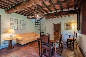 A cozy room with a wooden ceiling, a sofa, a dining table with chairs, a lamp, and framed pictures on the wall. - Apartment 'Casa Grande' with Mountain View, Shared Pool and Wi-Fi (Pietrabuona)