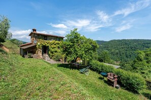 A rustic stone house with a sloped roof, a small porch, and a dining area with outdoor furniture. - Apartment 'Casa Grande' with Mountain View, Shared Pool and Wi-Fi (Pietrabuona)