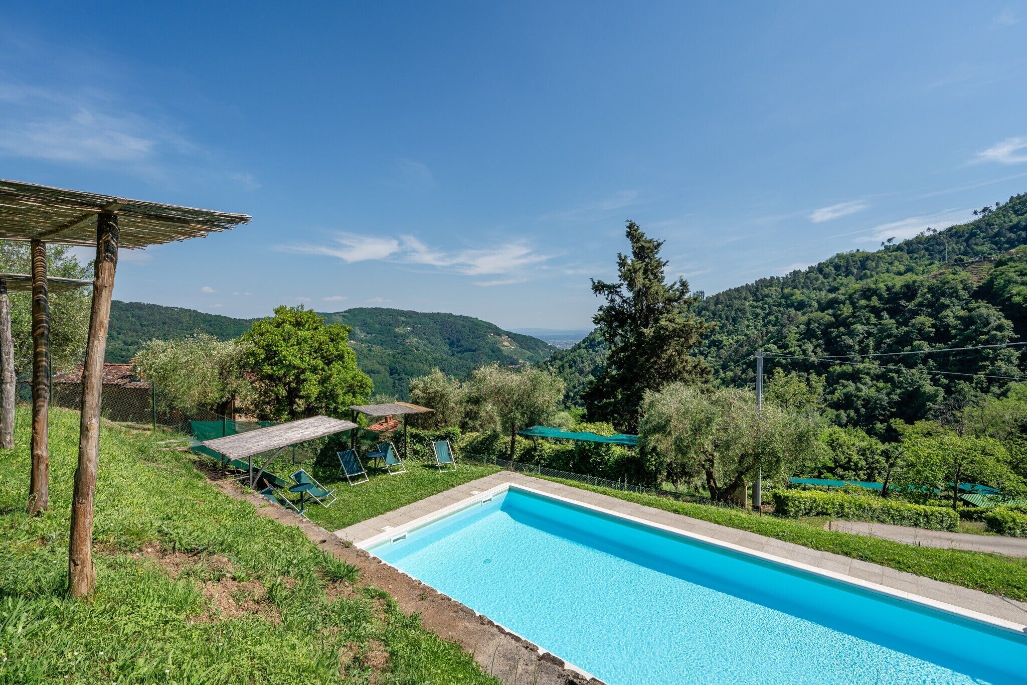 Piscina com deck de madeira, rodeada por vegetação e colinas.