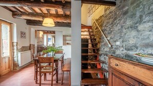 A rustic interior with exposed wooden beams, a stone wall, a wooden staircase, and a dining area with chairs and a table. - Casetta di Zano with Mountain View, Shared Pool and Wi-Fi (Pietrabuona)