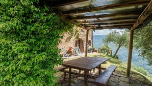 A rustic outdoor seating area with a wooden table and benches, surrounded by lush greenery and overlooking a mountainous landscape. - Casetta di Zano with Mountain View, Shared Pool and Wi-Fi (Pietrabuona)