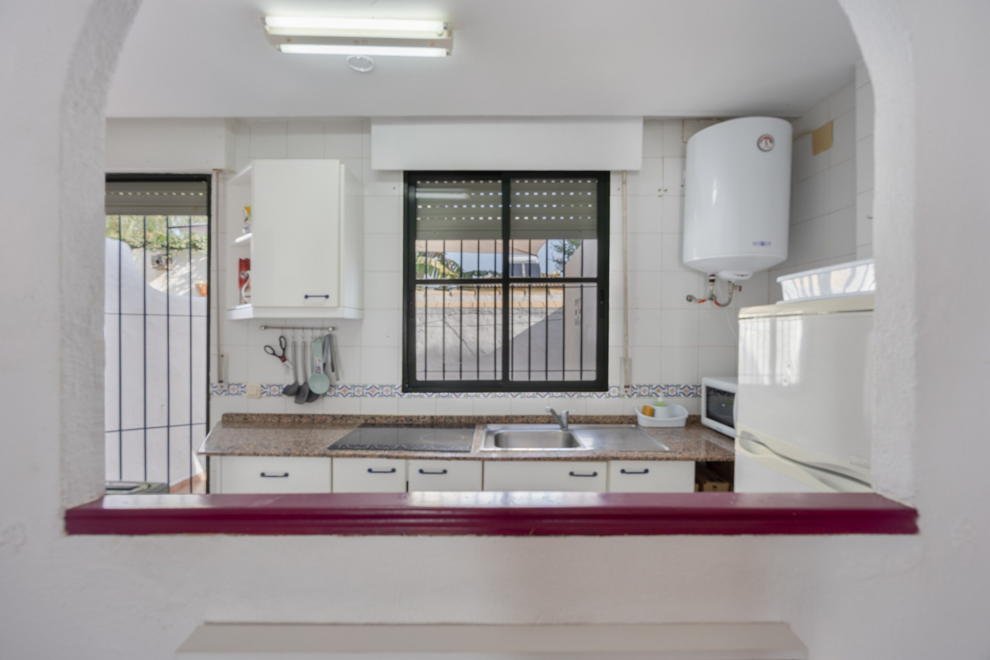Una cocina con armarios blancos, un lavamanos de acero inoxidable, un microondas y un calentador de agua.