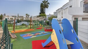 Une aire de jeux avec un toboggan, des balançoires et une structure d’escalade.