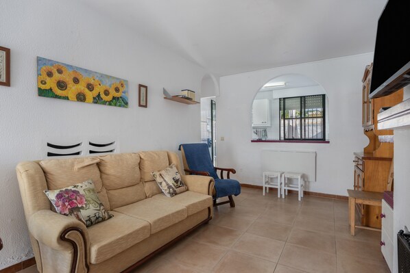 Un salón con un sofá color beige, un sillón azul, una mesita y una ventana con vistas.