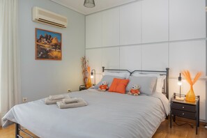 Un dormitorio con cama, almohadas, una mesita de noche, aire acondicionado, un cuadro en la pared y una mesita de noche con lámpara.