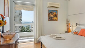 A hotel room with a bed, a window with curtains, a painting, an air conditioner, and a view of the outside.