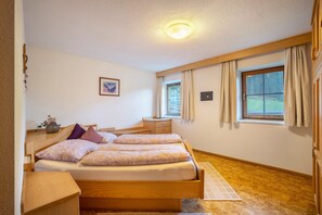 Makuuhuoneessa on puinen sänky, yöpöydät, yövalaisin, ikkuna, jossa on verhot, ja seinälle asennettu valaisin.