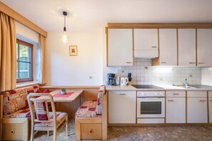 Kompakti keittiö, jossa on ruokailutila, puukaapit, sisäänrakennettu uuni ja ikkuna, jossa on verhot.
