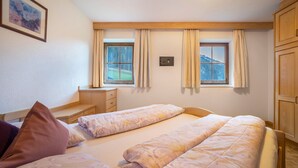 A bedroom with two beds, a desk, and a window with curtains.