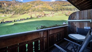 A wooden deck with a table and chairs, overlooking a green valley and mountains.