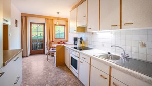 A kitchen with a sink, stove, and cabinets, a dining area with a table and chairs, and a large window with curtains.