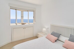 Een slaapkamer met een groot raam, een bed met kussens, een nachtkastje met een lamp en een radiator.