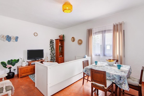 A compact living space with a TV, dining table, and a small kitchen area.