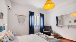 Une chambre d’hôtel comprenant un lit, une chaise, un climatiseur fixé au mur, une décoration en macramé suspendue et une étagère avec des articles de toilette.