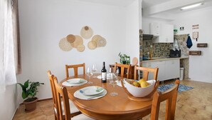 Un coin repas avec une table en bois, des chaises, un saladier de fruits, des verres à vin et une plante en pot.