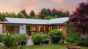 Une maison moderne dotée d’une grande véranda à l’avant, d’un patio couvert et d’un jardin bien entretenu.
