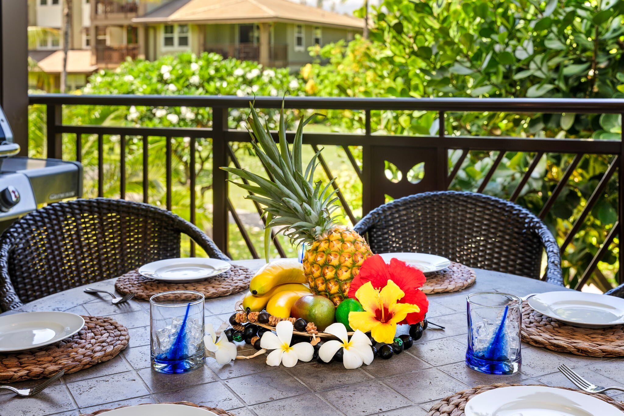 Une table dressée en plein air, ornée d’un arrangement de fruits tropicaux comprenant de l’ananas, des bananes et des mangues, et agrémentée d’un centre de table composé d’une fleur d’hibiscus.