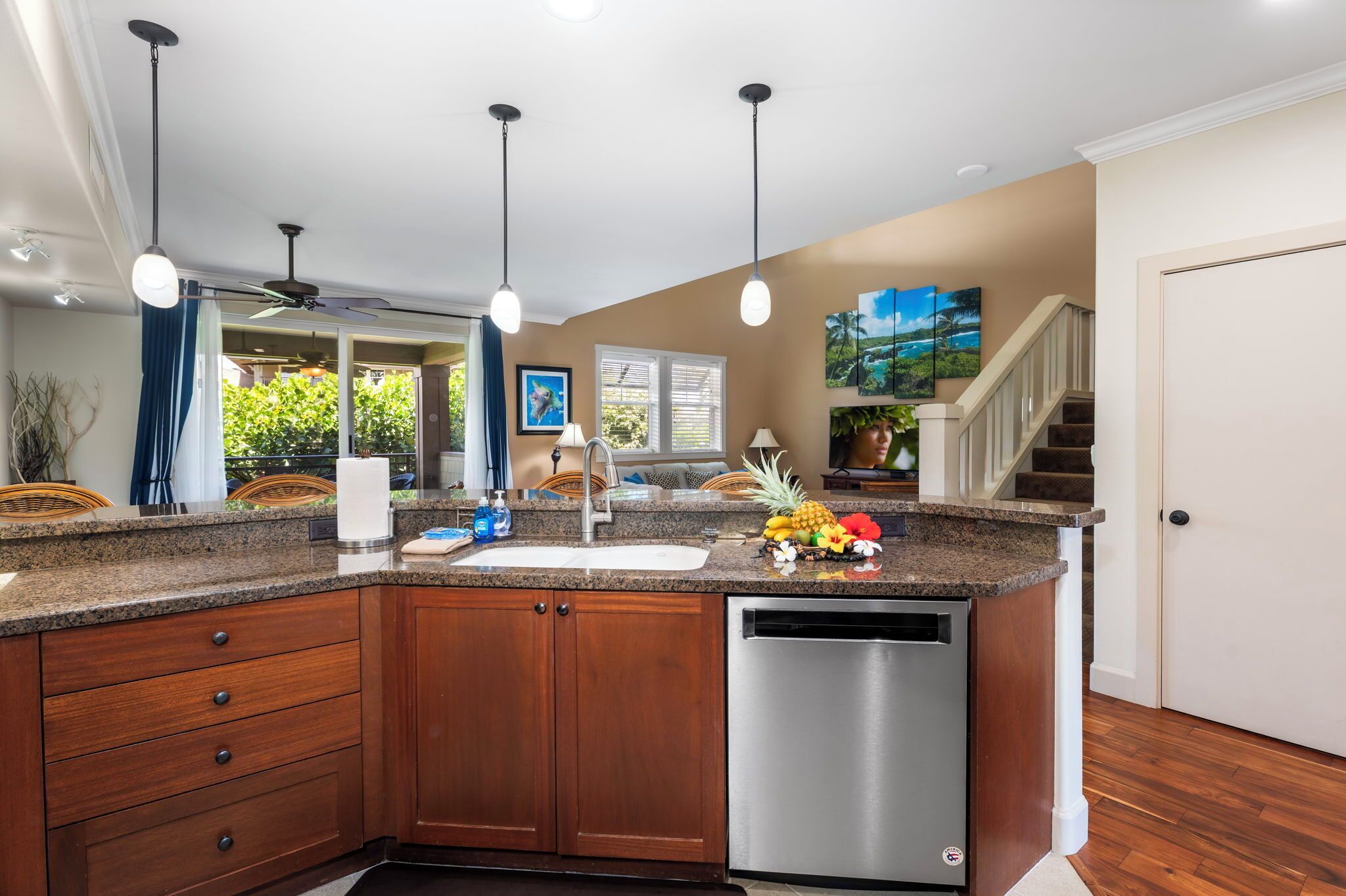 A kitchen with granite countertops, wooden cabinets, a stainless steel dishwasher, and pendant lighting.