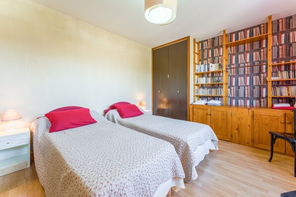 A bedroom with two beds, a wooden bookshelf, and a desk.
