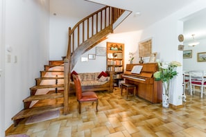Un escalier menant à un espace de vie comprenant un piano, des étagères et un canapé.