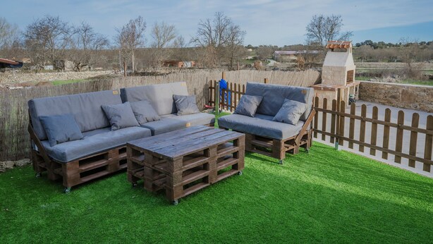 A patio with a wooden bench, two grey sofas, and a small wooden table. - Holiday Home 'La Isi' with Private Garden and Wi-Fi (Rades de Abajo)