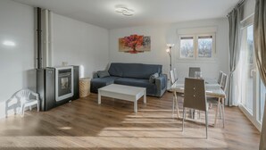 A living room with a sofa, a coffee table, a dining table with chairs, a painting on the wall, and a window with curtains. - Holiday Home 'La Isi' with Private Garden and Wi-Fi (Rades de Abajo)