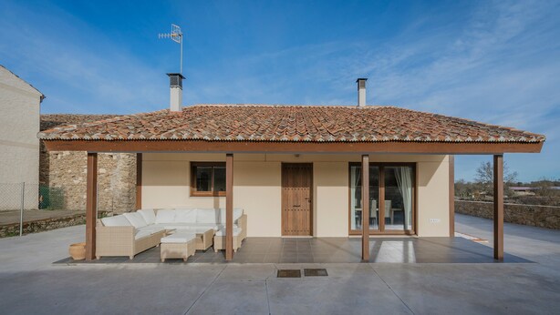 A modern house with a tiled roof, a covered patio with a sofa, and a wooden door.