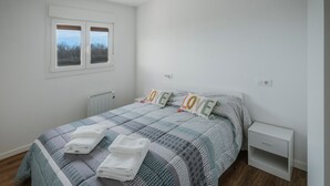 A bedroom with a bed, two bedside tables, a window, and a radiator.