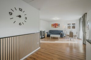 A modern living room with a large wall clock, a sofa, a coffee table, and a dining area with chairs. - Holiday Home 'La Isi' with Private Garden and Wi-Fi (Rades de Abajo)