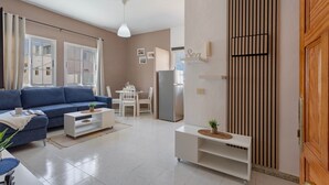 A modern living room with a sofa, a dining table, and a kitchen area with a refrigerator. - Vacation Home 'Bianco' with Shared Terrace and Wi-Fi (El Cotillo)