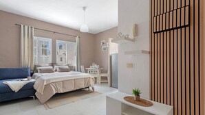 A modern bedroom with a bed, a blue sofa, a small table, and a wall-mounted phone. - Vacation Home 'Bianco' with Shared Terrace and Wi-Fi (El Cotillo)