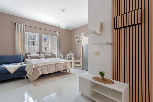 A modern bedroom with a bed, a blue sofa, a small table, and a wall-mounted phone.