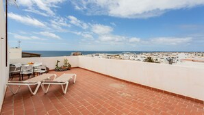 A rooftop terrace with white lounge chairs, a table, and potted plants. - Vacation Home 'Bianco' with Shared Terrace and Wi-Fi (El Cotillo)