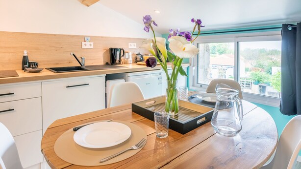 Une cuisine moderne avec des meubles blancs, un plan de travail en bois et une table à manger dressée avec des assiettes, des couverts et un vase de fleurs.