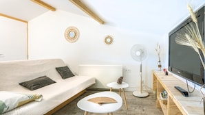 Un salon moderne comprenant un canapé, une petite table, un ventilateur, un téléviseur et des œuvres d’art décoratives accrochées au mur.